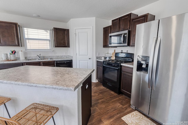 kitchen with a center island, black appliances, a kitchen bar, dark brown cabinetry, and dark wood-type flooring