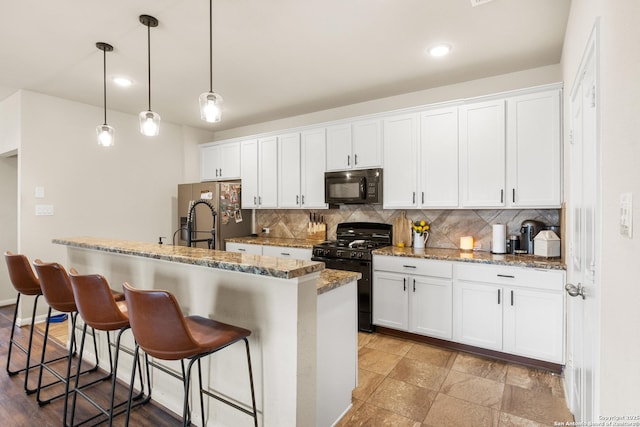 kitchen with pendant lighting, white cabinets, black appliances, an island with sink, and a breakfast bar area