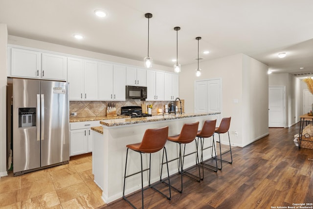 kitchen featuring stainless steel fridge, an island with sink, stove, pendant lighting, and white cabinets