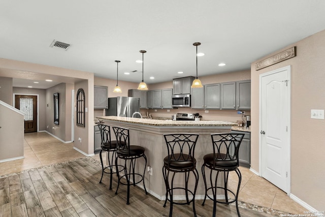 kitchen featuring appliances with stainless steel finishes, a kitchen bar, decorative light fixtures, gray cabinets, and a center island with sink