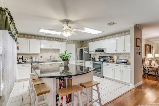 kitchen with a breakfast bar, white cabinetry, appliances with stainless steel finishes, and a skylight