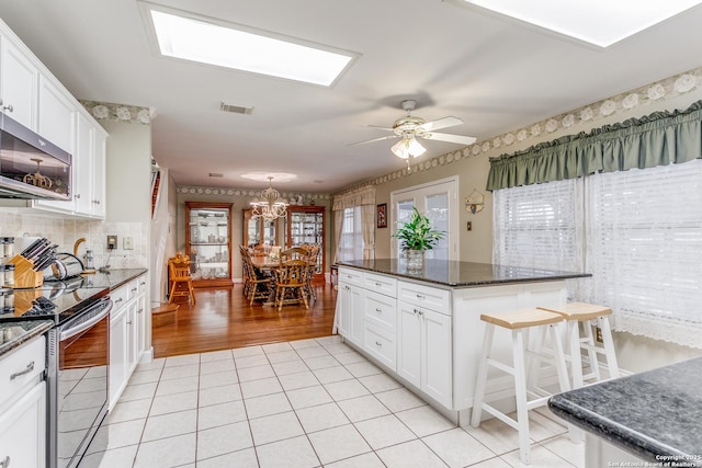 kitchen featuring white cabinets, a kitchen breakfast bar, ceiling fan with notable chandelier, and stainless steel appliances