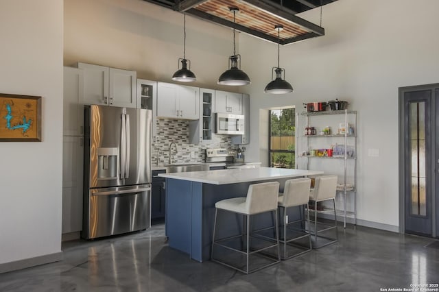 kitchen featuring a towering ceiling, tasteful backsplash, white cabinets, pendant lighting, and stainless steel appliances