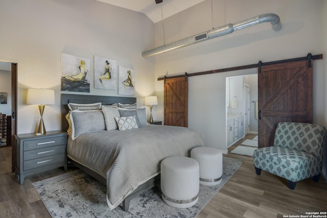 bedroom featuring hardwood / wood-style flooring, connected bathroom, high vaulted ceiling, and a barn door