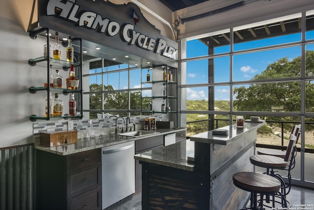 bar with sink, stainless steel dishwasher, expansive windows, and stone counters