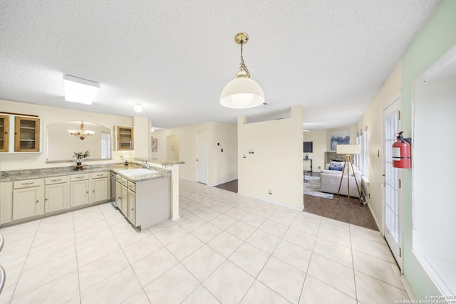 kitchen with an inviting chandelier, kitchen peninsula, a textured ceiling, pendant lighting, and sink