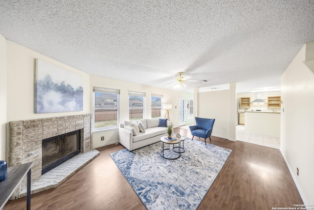 living room featuring ceiling fan, a fireplace, a textured ceiling, and dark hardwood / wood-style floors