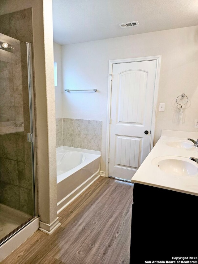 bathroom with hardwood / wood-style flooring, vanity, and plus walk in shower