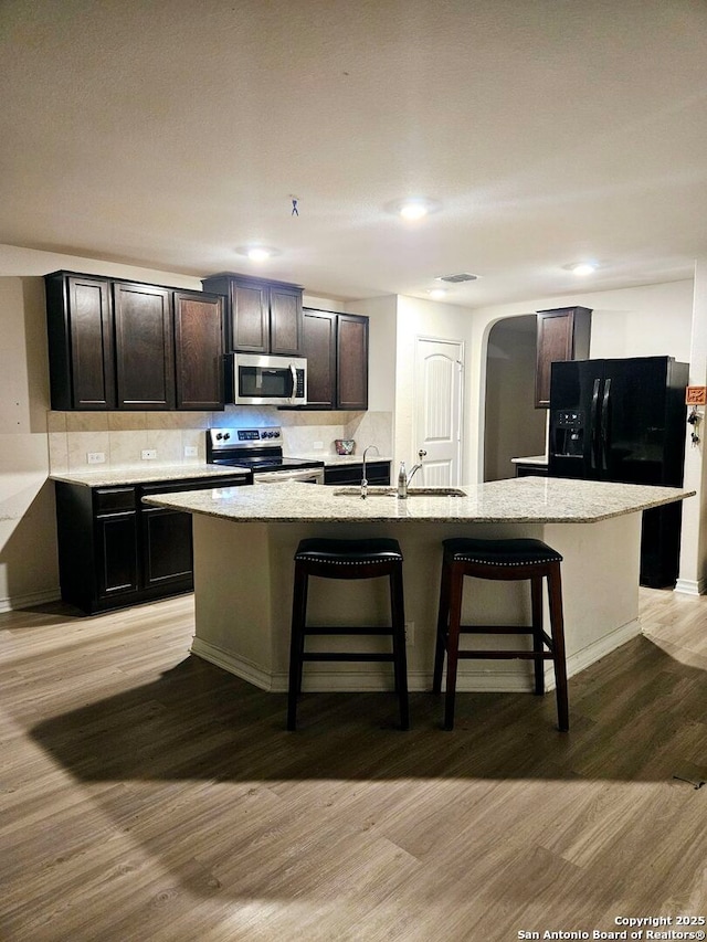 kitchen with light wood-type flooring, a kitchen island with sink, and stainless steel appliances