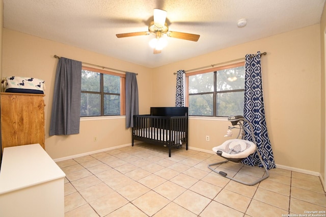 tiled bedroom featuring a textured ceiling, ceiling fan, and a nursery area