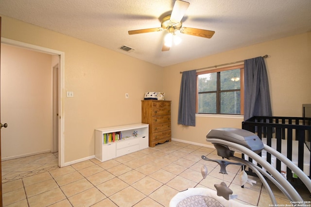 tiled bedroom featuring ceiling fan, a crib, and a textured ceiling