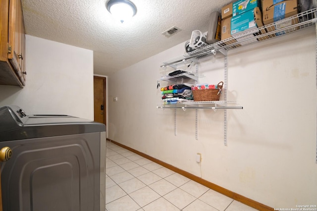 washroom with light tile patterned floors, washing machine and dryer, a textured ceiling, and cabinets