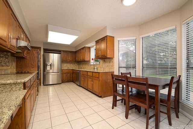 kitchen with light tile patterned floors, backsplash, light stone countertops, and stainless steel appliances