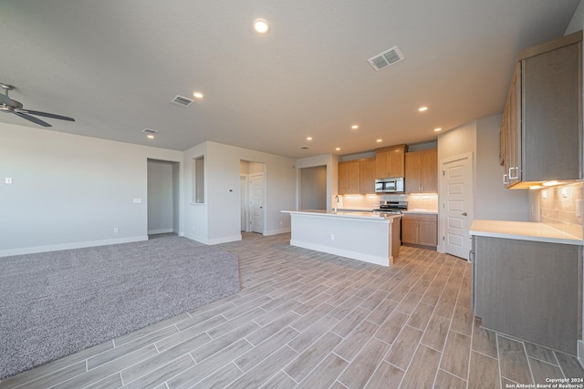 kitchen with ceiling fan, backsplash, stainless steel appliances, and a center island with sink