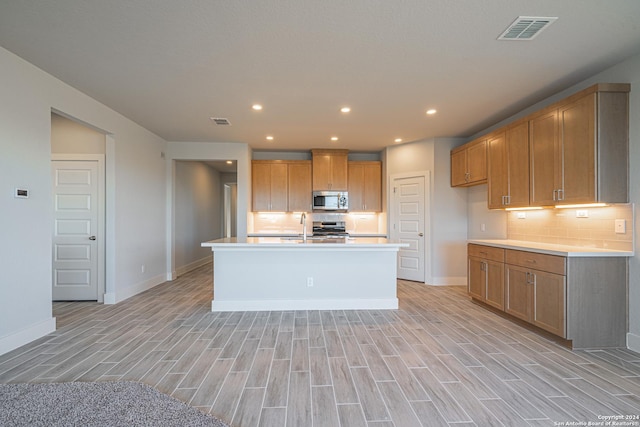 kitchen with tasteful backsplash, light hardwood / wood-style flooring, stainless steel appliances, and an island with sink