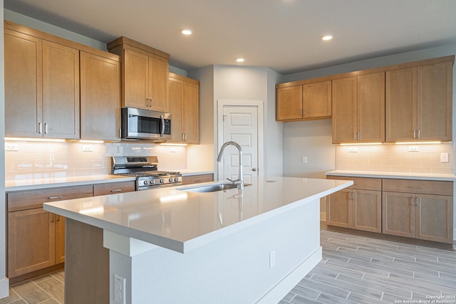 kitchen with stainless steel appliances, sink, decorative backsplash, and a kitchen island with sink