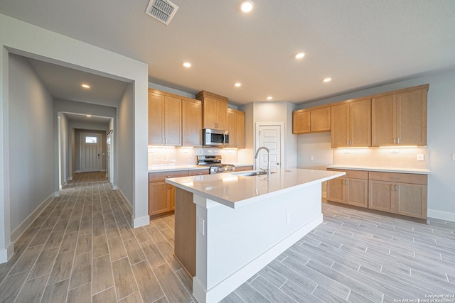 kitchen featuring stainless steel appliances, backsplash, a center island with sink, and sink