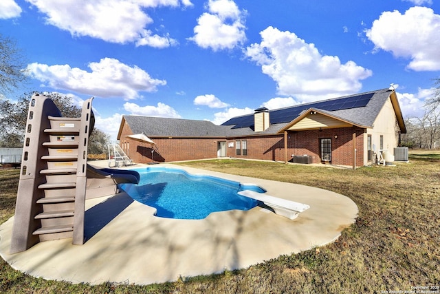 view of pool featuring central AC unit, a diving board, a yard, and a water slide