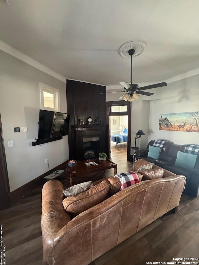 living room featuring dark wood-type flooring, crown molding, a fireplace, and ceiling fan