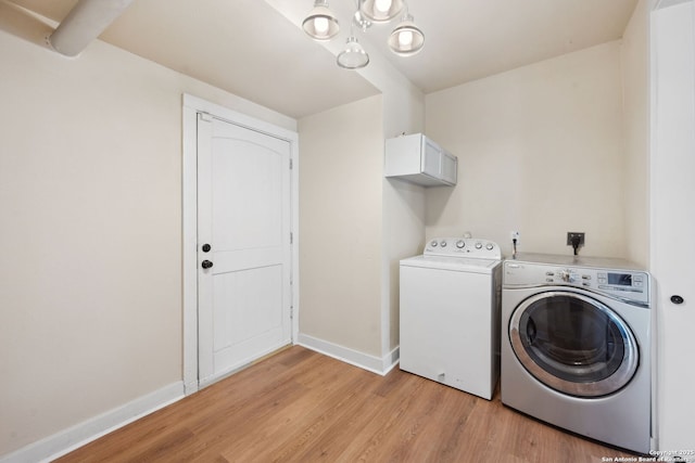 washroom featuring laundry area, washing machine and dryer, light wood-type flooring, baseboards, and a notable chandelier