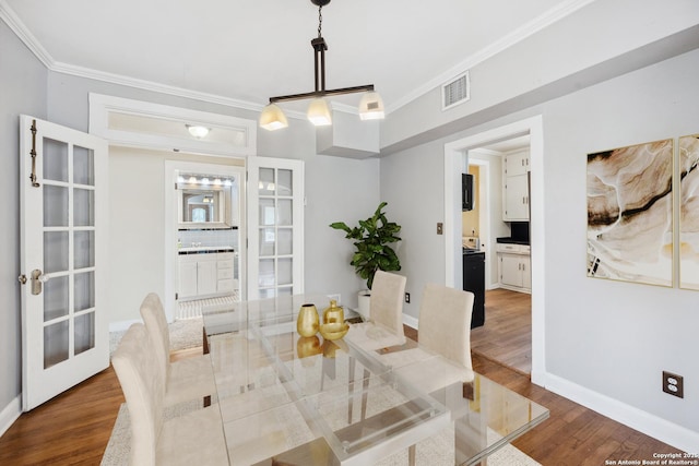 dining space featuring visible vents, ornamental molding, wood finished floors, baseboards, and french doors
