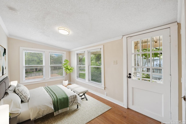 bedroom featuring multiple windows, a textured ceiling, baseboards, wood finished floors, and lofted ceiling