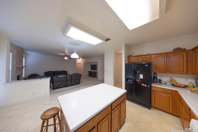 kitchen with ceiling fan, a breakfast bar, a kitchen island, and black fridge with ice dispenser