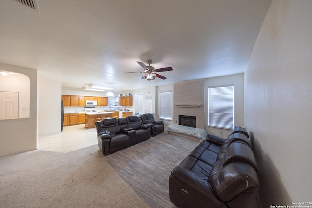 living room featuring ceiling fan, light colored carpet, and a brick fireplace