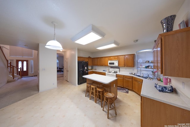 kitchen featuring a kitchen island, a breakfast bar, sink, white appliances, and hanging light fixtures