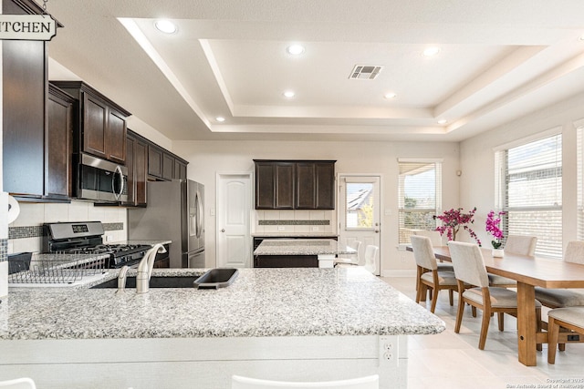 kitchen featuring a tray ceiling, light stone countertops, backsplash, and appliances with stainless steel finishes