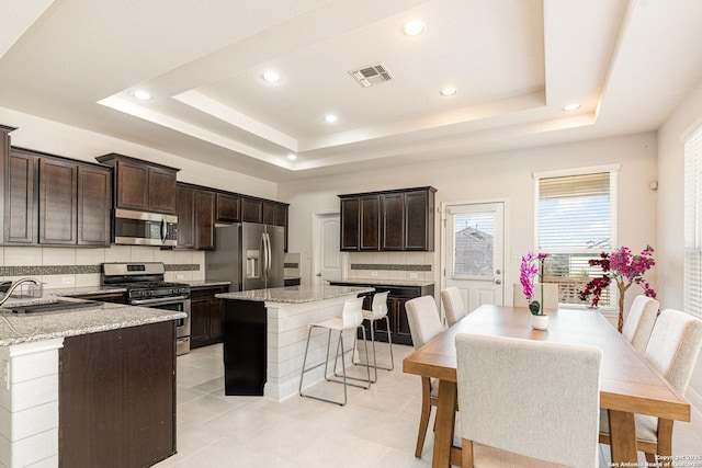 kitchen featuring appliances with stainless steel finishes, light stone counters, a tray ceiling, and a center island