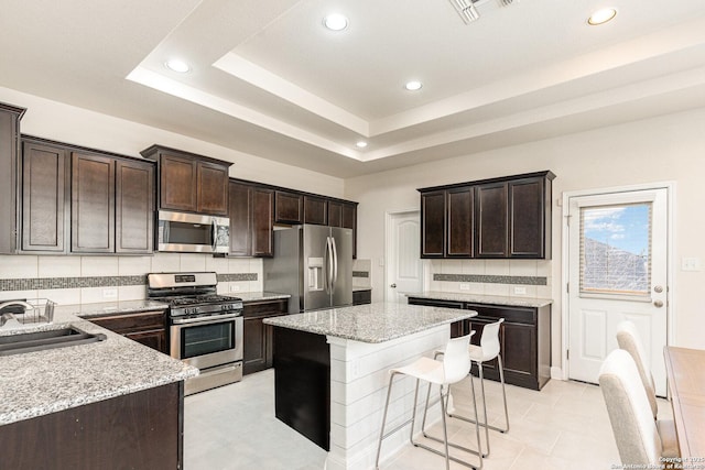 kitchen featuring stainless steel appliances, sink, backsplash, light stone counters, and a tray ceiling