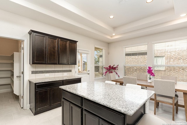 kitchen featuring light stone counters, dark brown cabinetry, a center island, and a raised ceiling