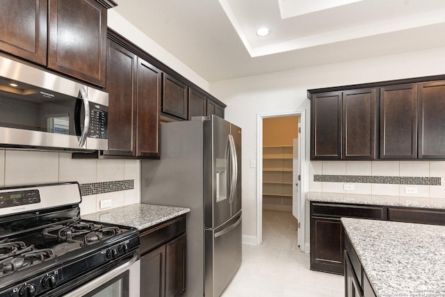 kitchen featuring decorative backsplash, light stone counters, stainless steel appliances, and dark brown cabinetry