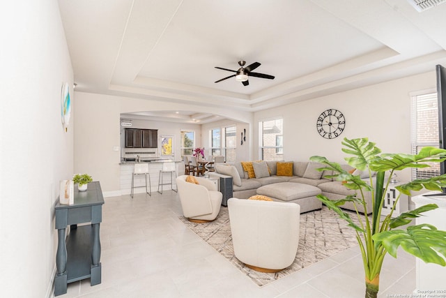 living room featuring ceiling fan, light tile patterned floors, and a tray ceiling