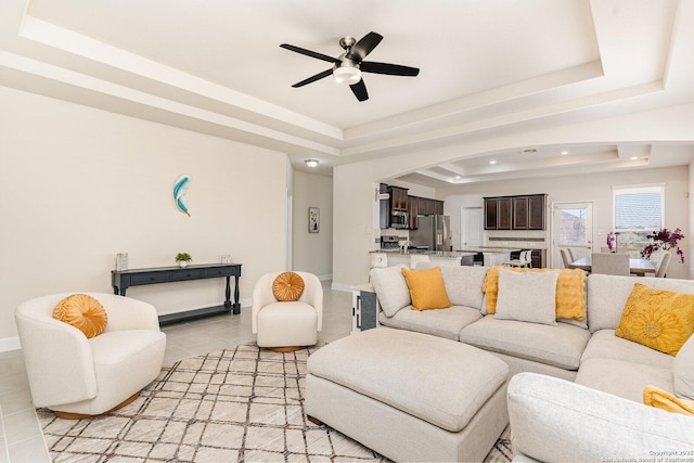 living room featuring a raised ceiling, ceiling fan, and light tile patterned flooring