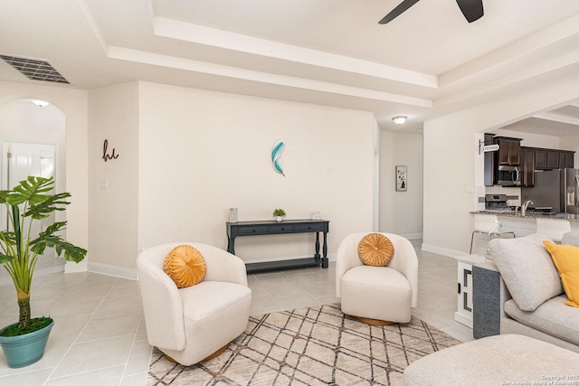 tiled living room featuring ceiling fan, sink, and a tray ceiling