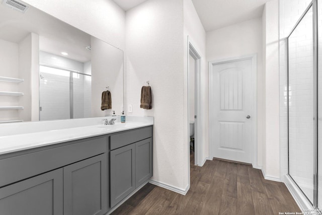 bathroom with toilet, hardwood / wood-style floors, a shower with door, and vanity