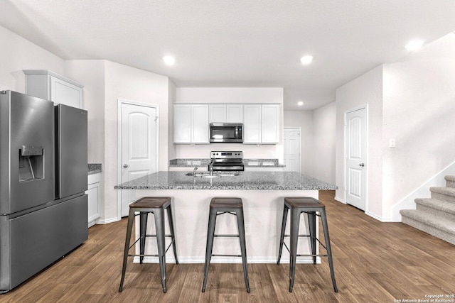 kitchen featuring dark wood-type flooring, white cabinetry, stainless steel appliances, and an island with sink