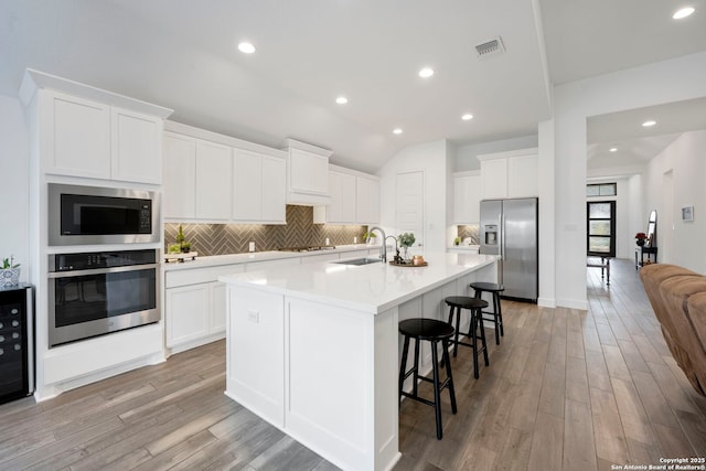 kitchen with stainless steel appliances, sink, a center island with sink, and white cabinets