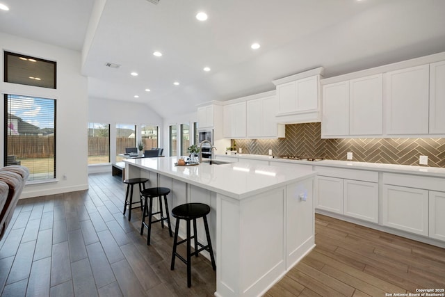 kitchen featuring white cabinetry, vaulted ceiling, sink, and a center island with sink