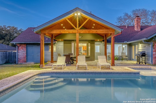 pool at dusk featuring grilling area, ceiling fan, and a patio area