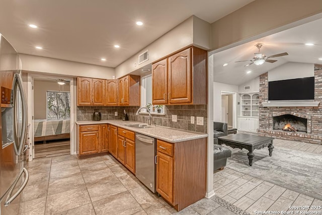 kitchen featuring lofted ceiling, a brick fireplace, decorative backsplash, sink, and appliances with stainless steel finishes