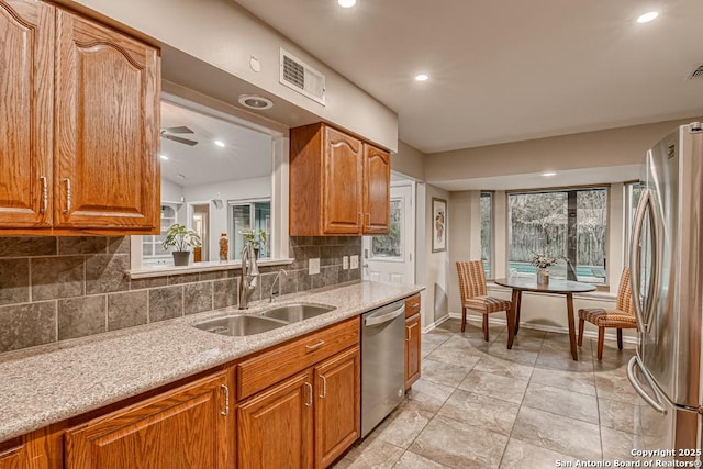 kitchen featuring stainless steel appliances, tasteful backsplash, ceiling fan, sink, and light stone counters