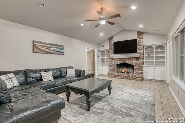 living room featuring lofted ceiling, a fireplace, built in features, light wood-type flooring, and ceiling fan