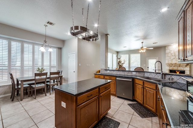 kitchen featuring a stone fireplace, ceiling fan with notable chandelier, sink, stainless steel dishwasher, and a textured ceiling