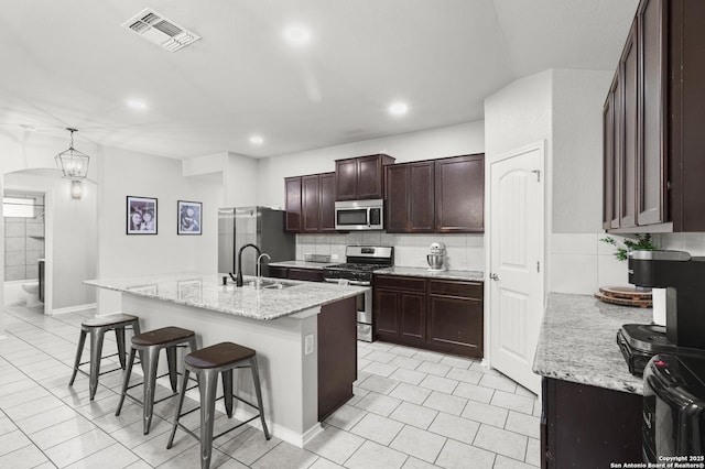 kitchen with light stone countertops, appliances with stainless steel finishes, decorative light fixtures, an island with sink, and a breakfast bar area