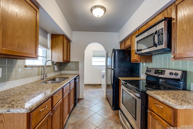 kitchen with light tile patterned floors, stainless steel appliances, backsplash, light stone counters, and sink