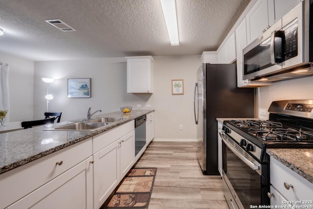 kitchen with light stone countertops, a textured ceiling, white cabinetry, stainless steel appliances, and sink