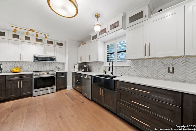 kitchen featuring white cabinetry, appliances with stainless steel finishes, decorative light fixtures, light wood-type flooring, and sink